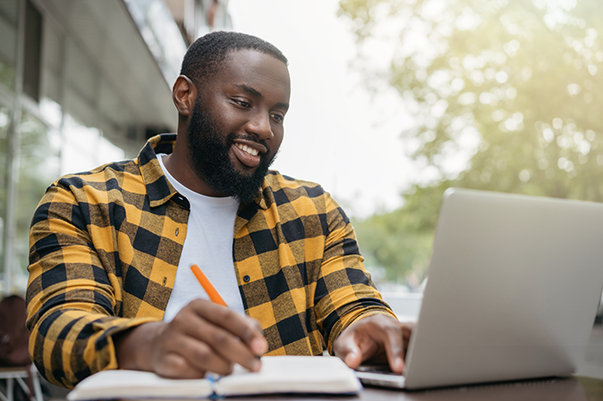 Young black american taking notes while working on a laptop outside