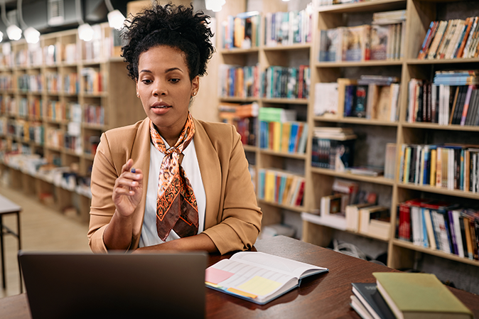 Middle woman in a library teaching an online class with her laptop