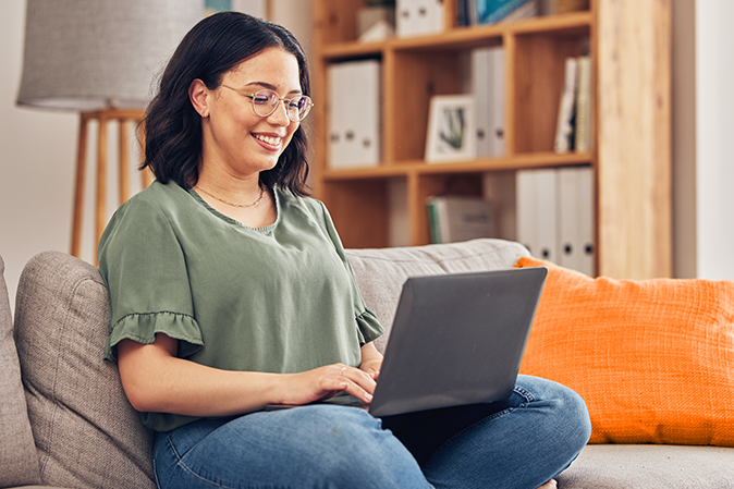 Young woman smiling while working on a laptop sitting on the couch in her living room
